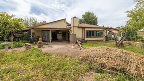 A single-story house with a covered patio, a garage, and a yard with various plants and a pile of hay. - Mesa Meadow Retreat (Mesa)