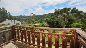 Une balustrade en bois surplombe un paysage luxuriant, avec des arbres et une maison située au loin.