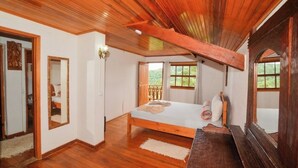 Une chambre avec un plafond en bois, un lit avec des oreillers, un miroir et une fenêtre donnant sur un paysage verdoyant.
