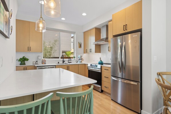 A modern kitchen with a large island, stainless steel appliances, wooden cabinets, and pendant lighting.