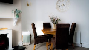 Un coin repas avec une table ronde en bois, quatre chaises marron à revêtement rembourré, un vase de fleurs, une horloge murale et une cheminée blanche.
