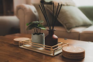 A wooden table with a tray holding a white ceramic pot with a plant, a dark brown vase with a reed diffuser, and two round coasters. - Centre of Whitley Bay Short & Long Stay (Whitley Bay)