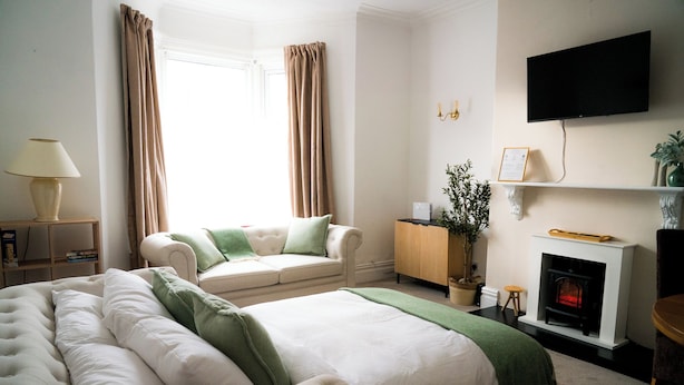 Une chambre d’hôtel avec un grand lit, un canapé, une cheminée, une télévision et une fenêtre avec des rideaux.