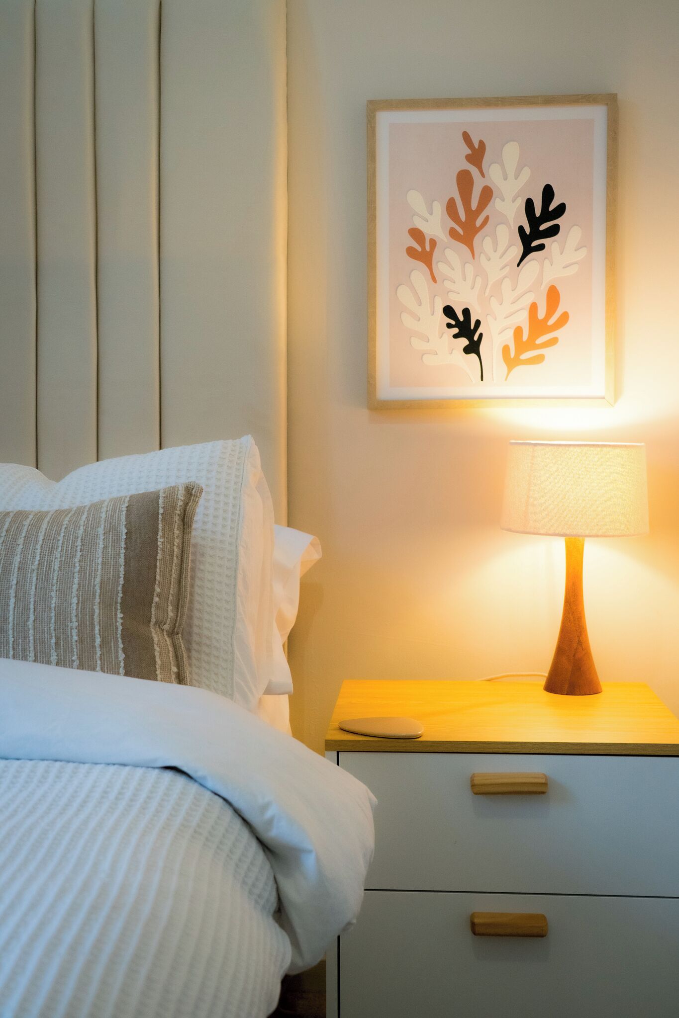 A neatly made bed with a striped pillow, a bedside table with a lamp, and a framed artwork on the wall.