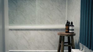 Une salle de bain avec un mur en marbre, un tabouret en bois et des articles de toilette posés dessus.