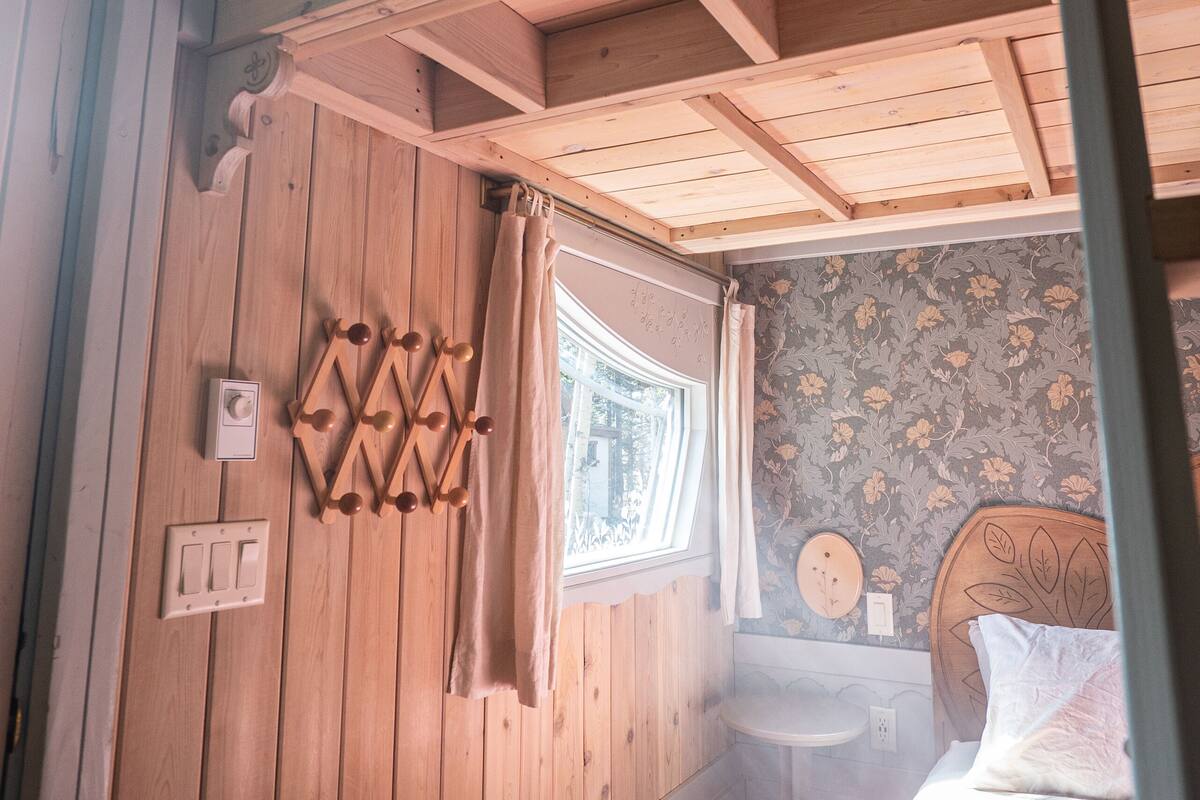 A wooden room with a bed, a small table, and a window with curtains.