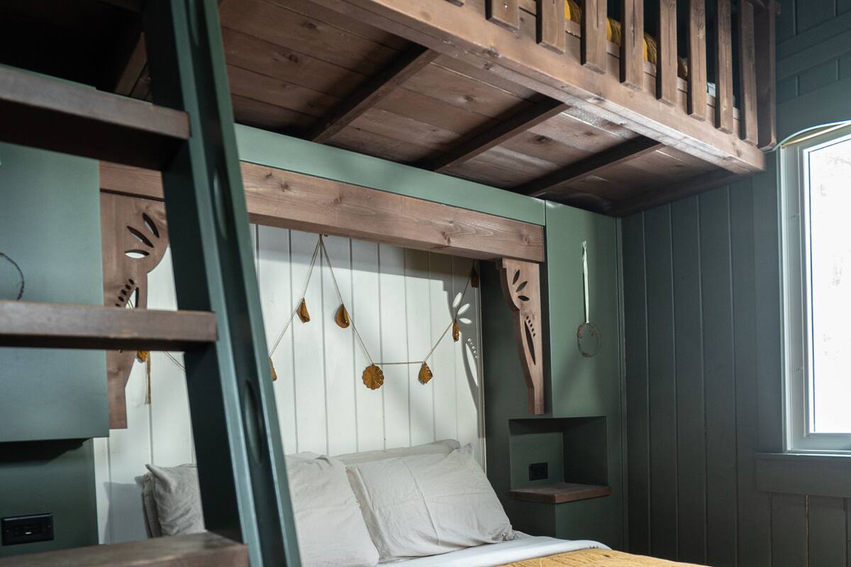 A bunk bed with a wooden ladder, a headboard with hanging decorations, and a window with daylight.