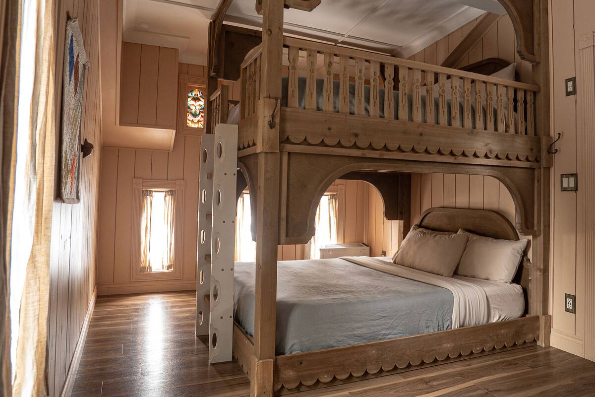 A wooden bunk bed with a balcony, a wooden floor, and a window with curtains.