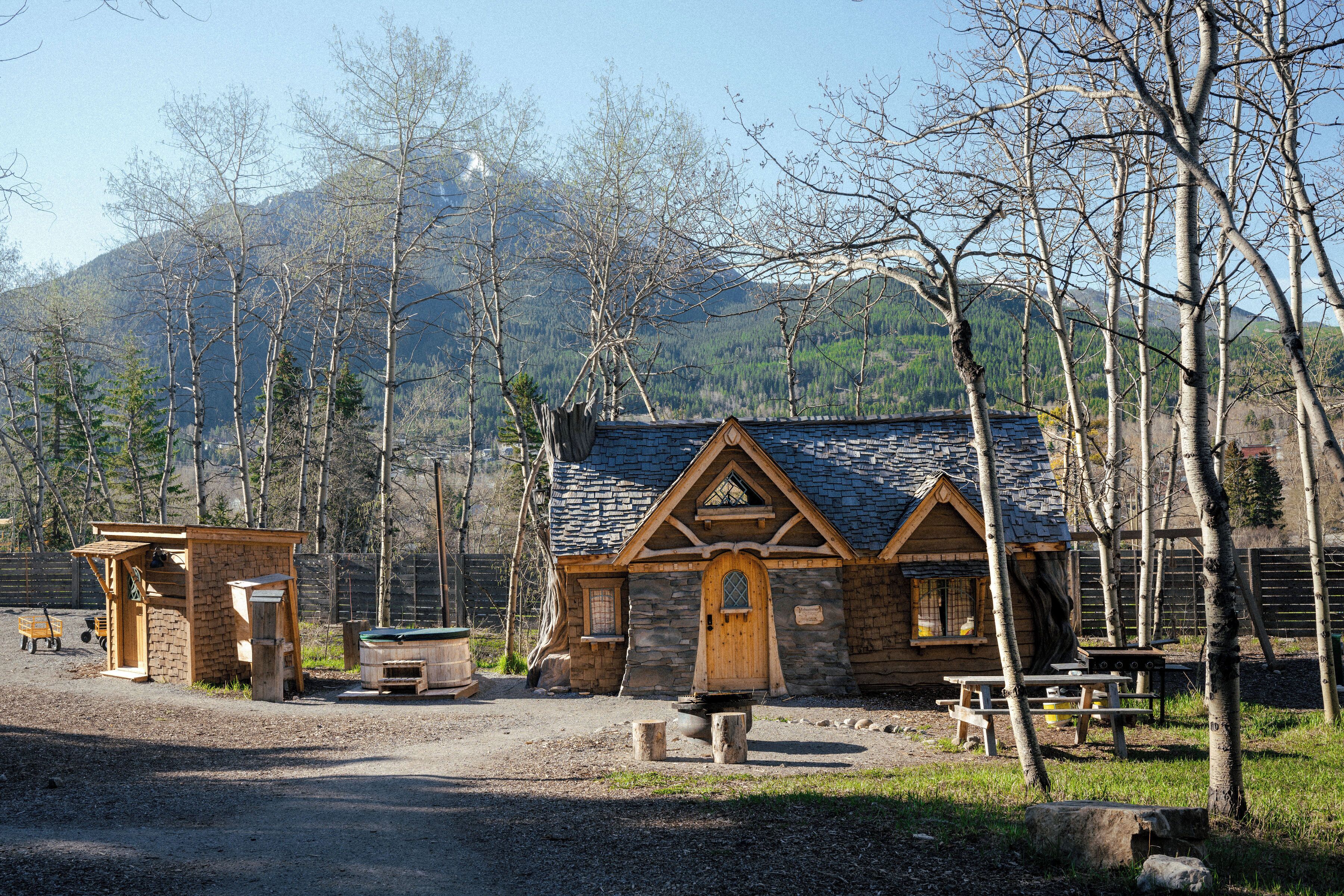 Eine rustikale Holzhütte mit Natursteinfassade und Holzelementen, umgeben von einer natürlichen Landschaft mit Bäumen und Bergen im Hintergrund.