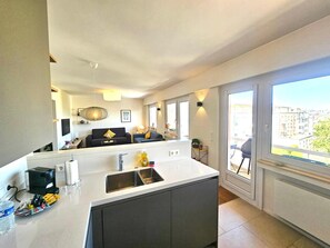 Una cocina moderna con una isla central, una zona de comedor con sofá y un amplio ventanal con vistas a la ciudad.
