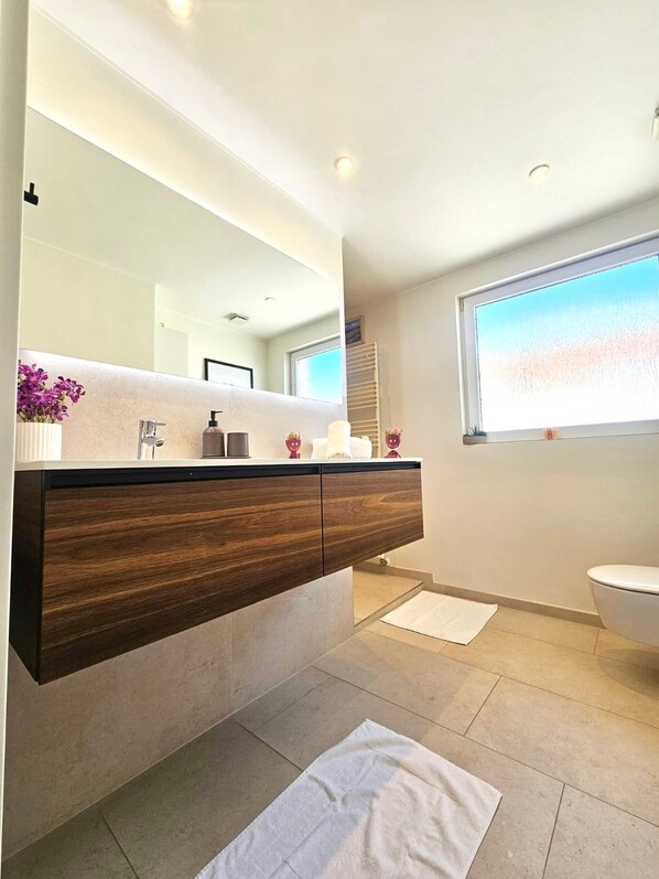 Un baño moderno con un espejo grande, tocador de madera y un inodoro.