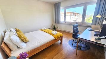 Habitación de hotel con cama, escritorio, silla, ventana con vistas y una planta en maceta.