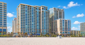 A high-rise hotel with multiple balconies, a sandy beach in the foreground, and palm trees. - Virginia Beach | Coastal Getaway | Resort Pool & Beach Access (Virginia Beach)