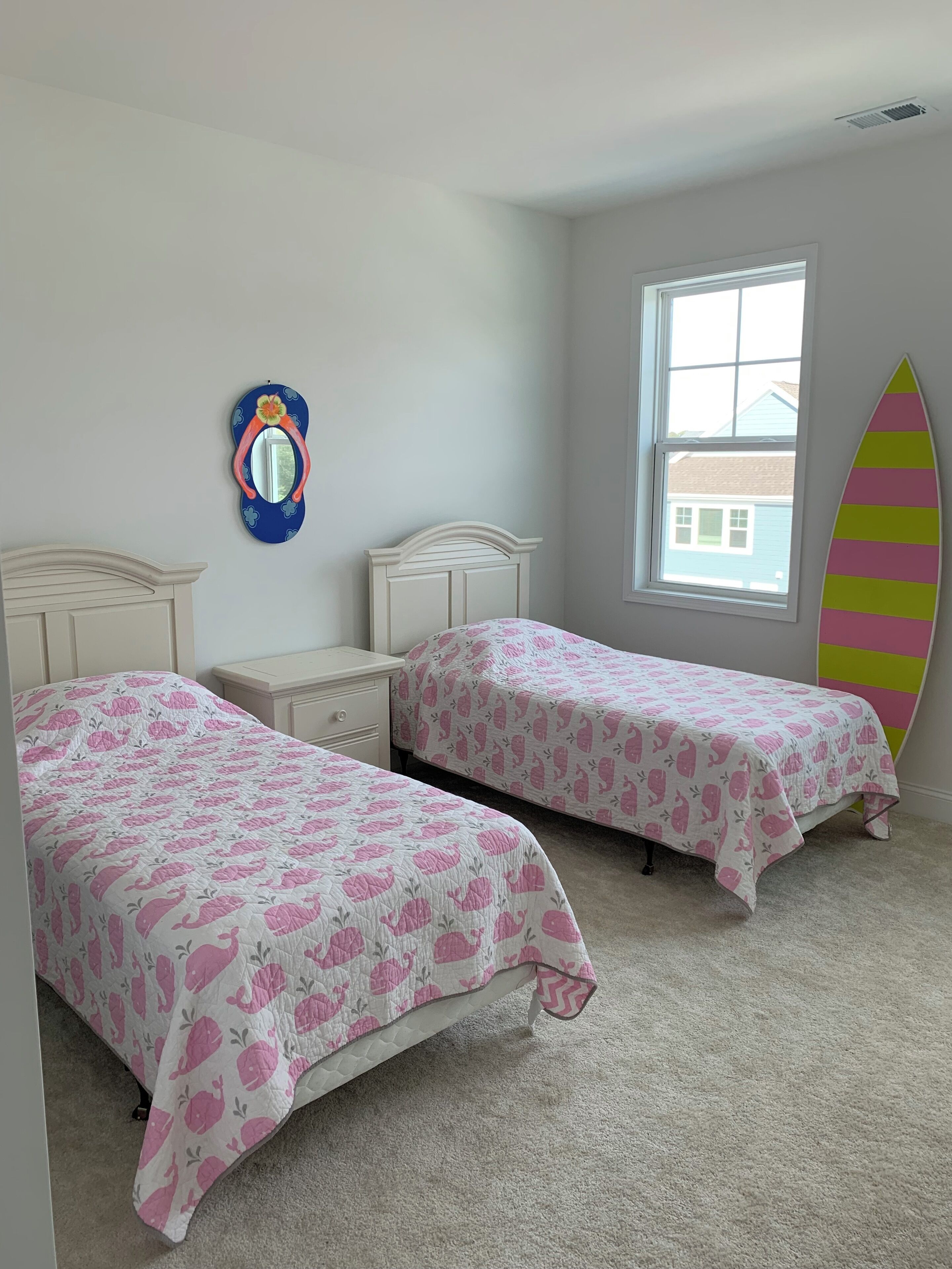 A bedroom with two beds, a window, a surfboard decoration, and a mirror with a flip-flop design.