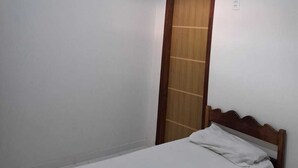 Una stanza piccola e pulita con un letto singolo, una porta di legno e un condizionatore d'aria a parete.
