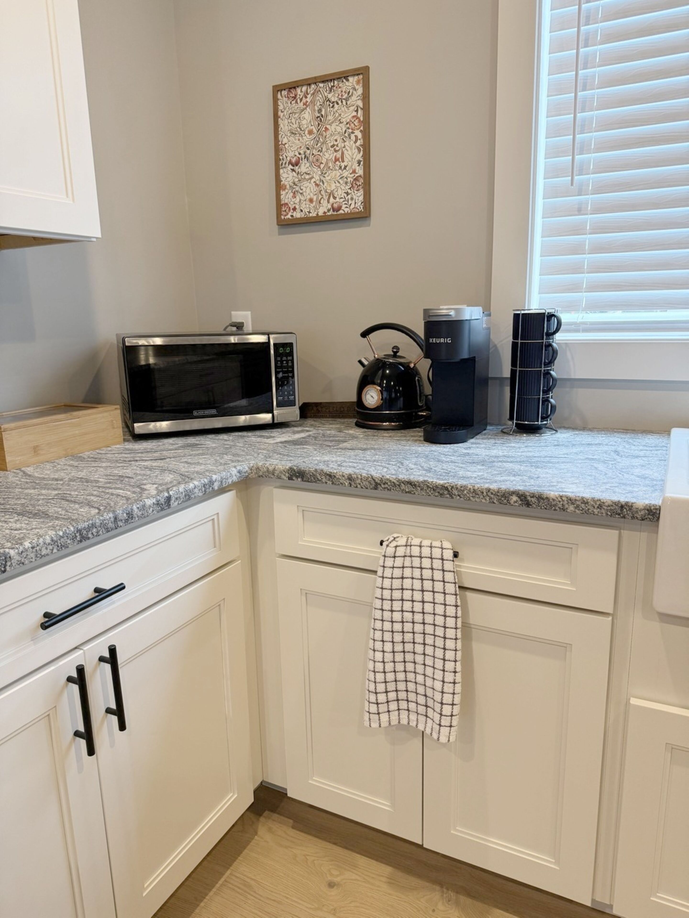 A kitchen with white cabinets, a microwave, a kettle, and a coffee maker.