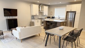 Una cocina moderna con armarios blancos, un refrigerador de acero inoxidable y un comedor con una mesa de madera y sillas negras.