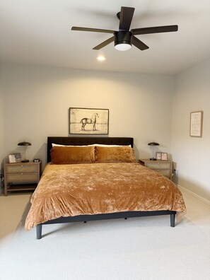 A bedroom with a bed, a ceiling fan, bedside tables, and a framed picture on the wall.