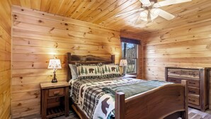 Une chambre dans une cabane en bois, avec un lit, deux tables de chevet, une commode et un ventilateur de plafond.