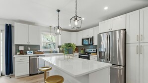 Una cocina moderna con armarios blancos, electrodomésticos de acero inoxidable y una isla central con taburetes.