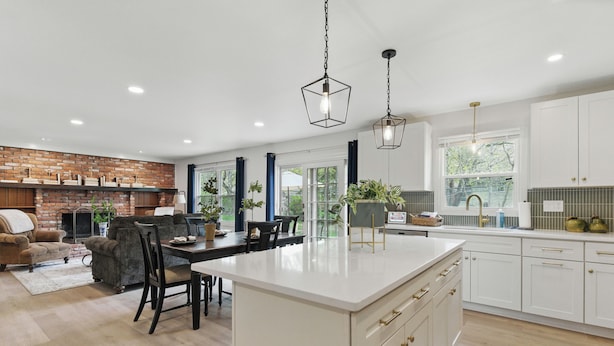 Una cocina amplia con una isla central, muebles blancos y una pared de ladrillo decorativa.