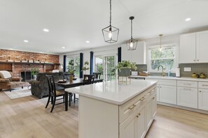 Una cocina amplia con una isla central, muebles blancos y una pared de ladrillo decorativa.