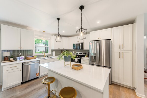 Una cocina moderna con armarios blancos, electrodomésticos de acero inoxidable y una isla central con taburetes.