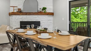 A dining area with a wooden table set for six, a white brick fireplace, and a view of greenery through a sliding glass door. - Once Upon A Trail: Direct Trail Access >1mi to OZ Bike Park >Hot Tub >Theater Rm (Bella Vista)