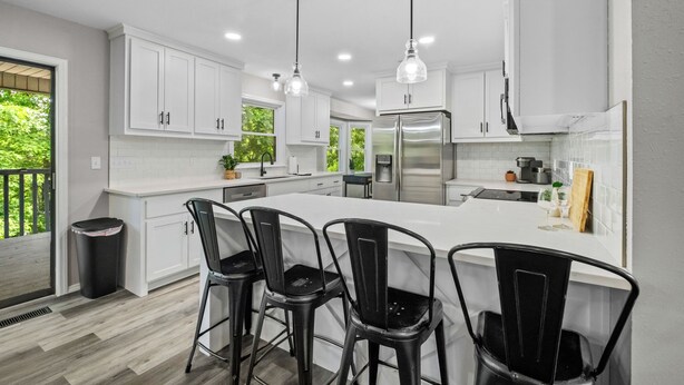 A modern kitchen with white cabinets, stainless steel appliances, and black bar stools. - Once Upon A Trail: Direct Trail Access >1mi to OZ Bike Park >Hot Tub >Theater Rm (Bella Vista)