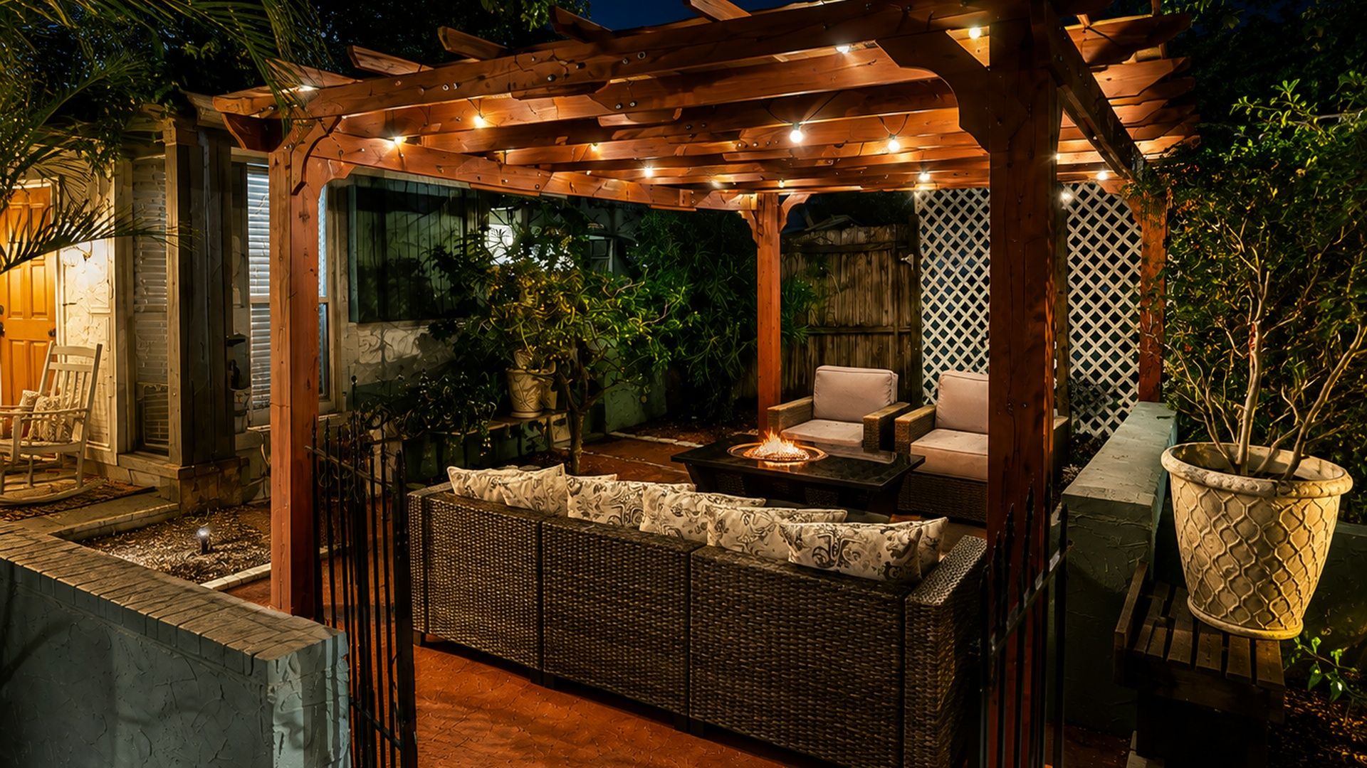 Eine Terrassenfläche im Freien mit einer Pergola, Korbmöbeln und Kübelpflanzen.