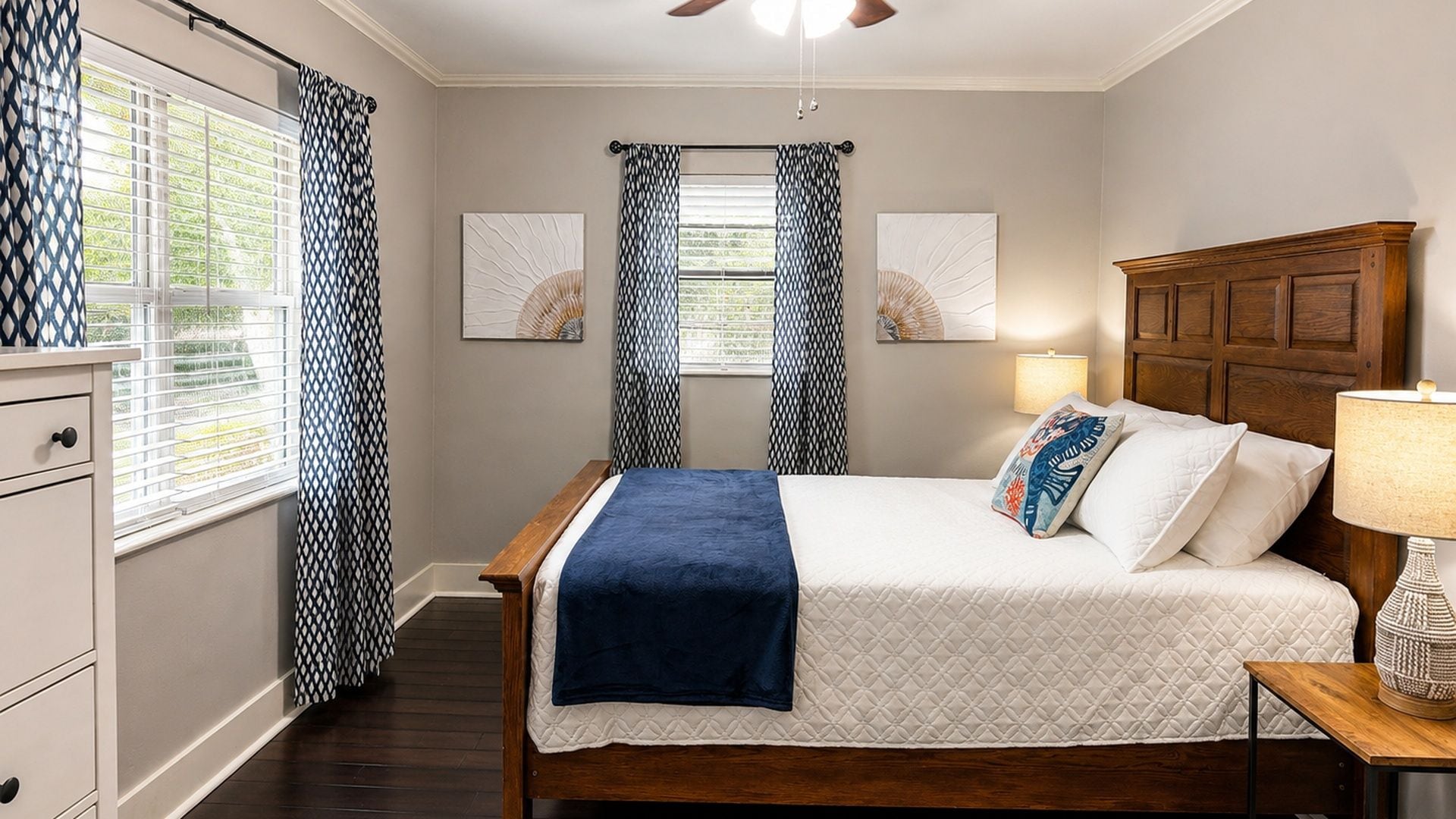 A bedroom with a bed, curtains, a nightstand, a lamp, and artwork on the wall.
