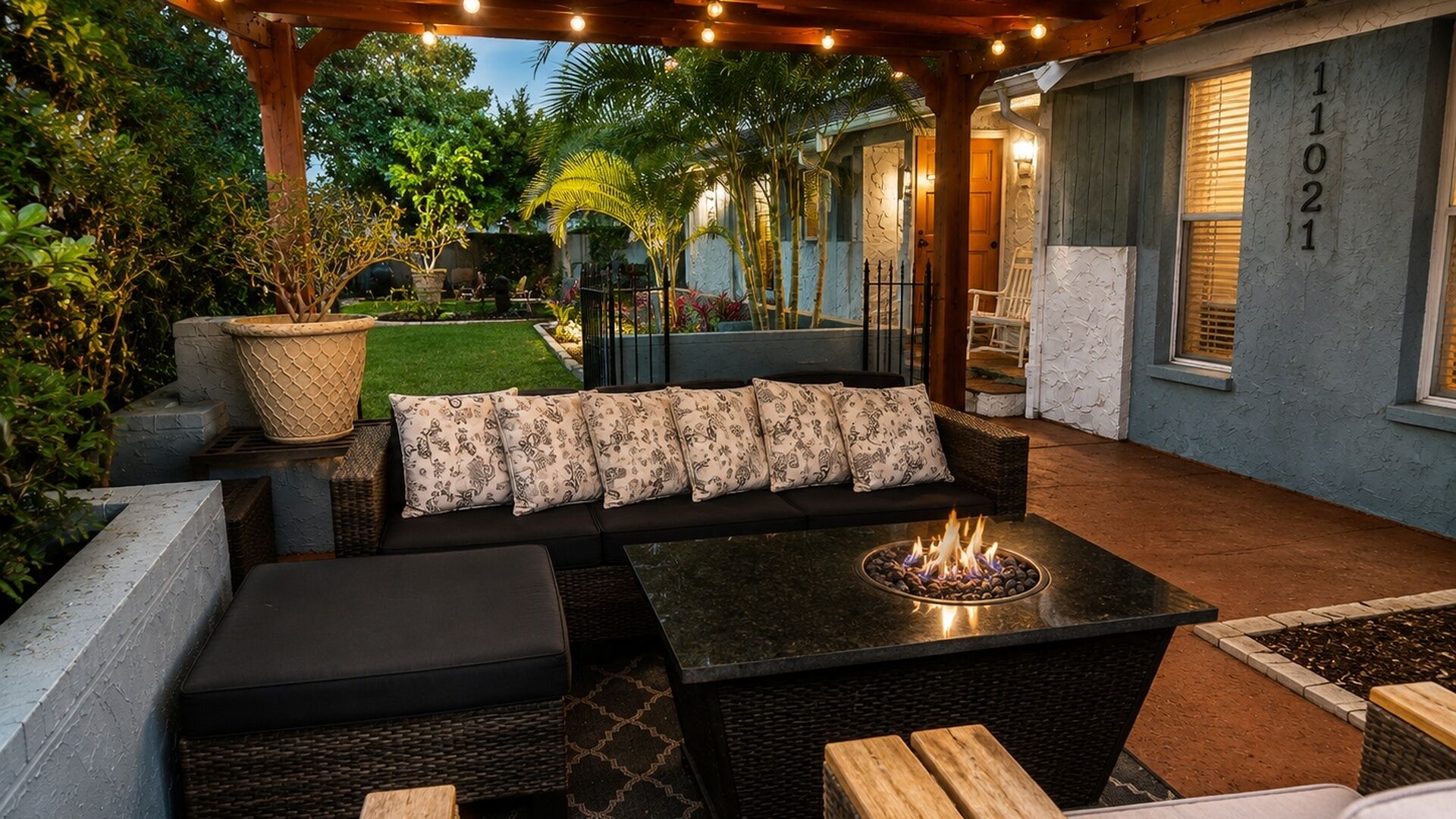 Ein Patio im Freien mit Feuerstelle, Sitzgelegenheiten und einer Pergola mit Lichterketten.
