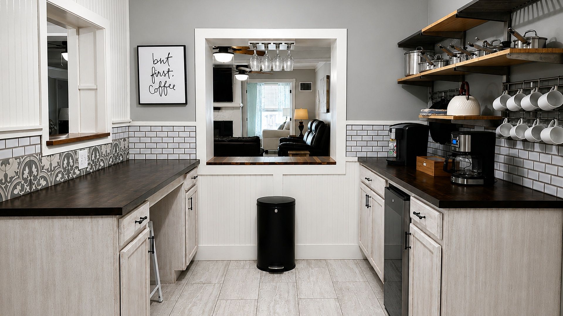 Una cocina con armarios blancos, un bote de basura negro y una cafetera.