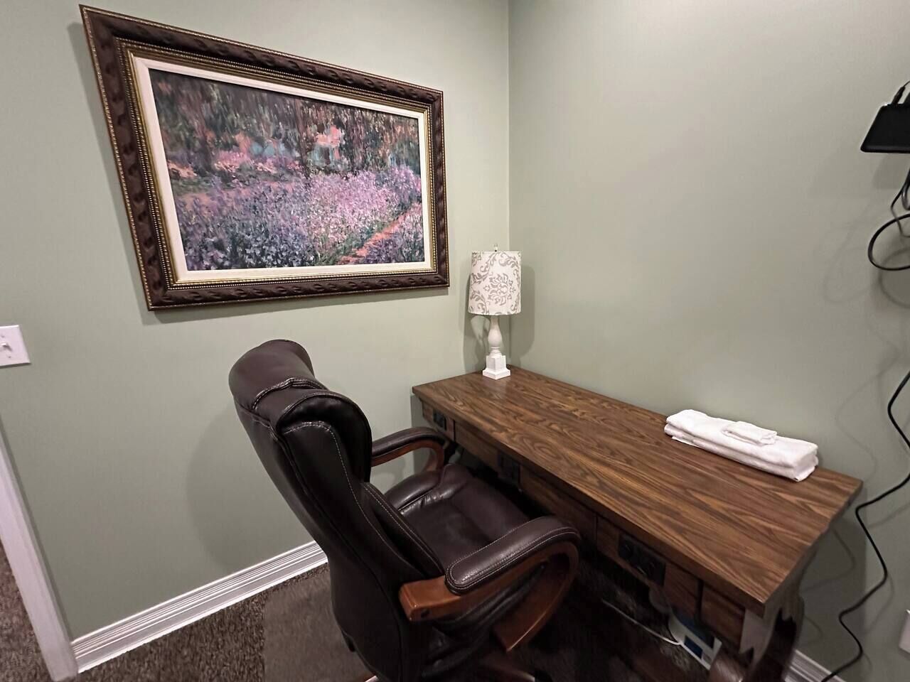 Une pièce avec un bureau en bois, un fauteuil en cuir, un tableau encadré et une lampe.