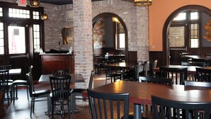 Een restaurantinterieur met bakstenen muren, houten tafels en zwarte stoelen.