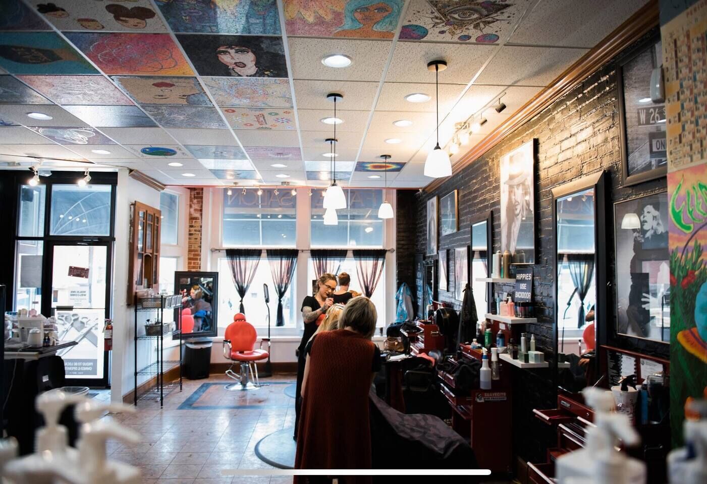 Un salón con una decoración moderna, que presenta una pared de ladrillo, ventanas amplias y un techo con obras de arte coloridas.