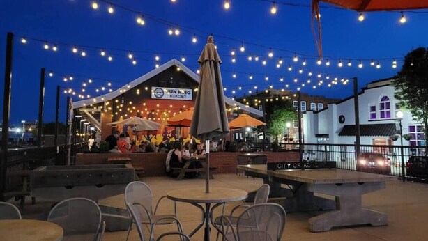 Een terras met tafels en stoelen, lichtslingers en parasols.
