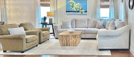Una sala de estar con un sofá beige, dos sillones, una mesa de centro de madera y un cuadro en la pared.