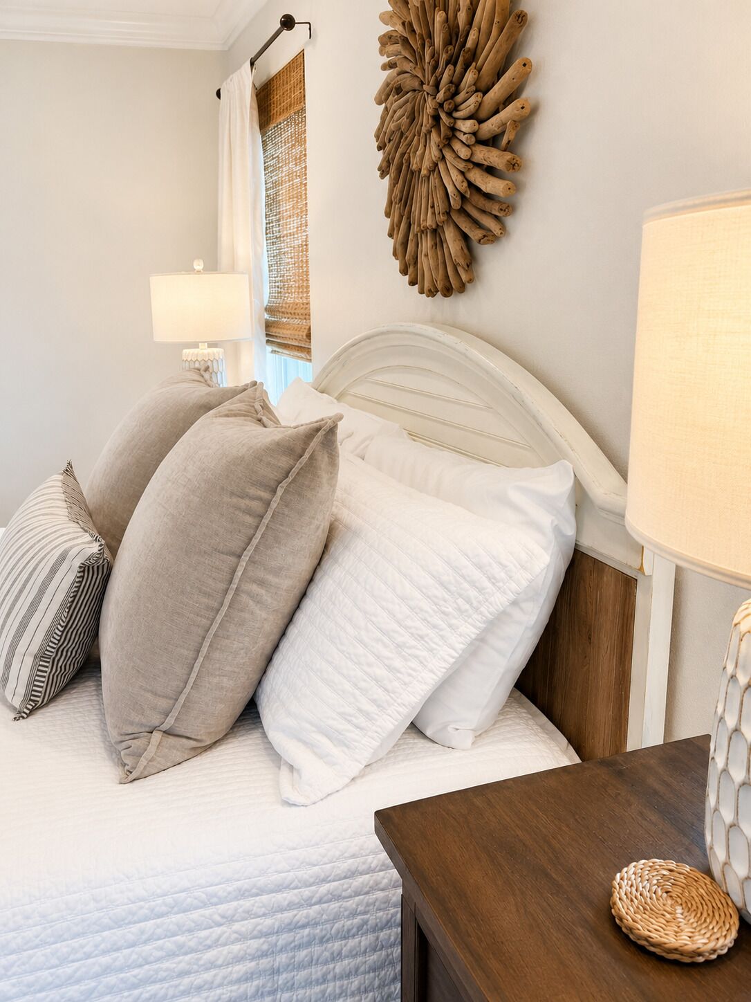 Una cama bien hecha con almohadas, una mesita de noche con lámpara y una decoración en la pared.