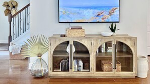 Una sala de estar con una mesa consola de madera, un televisor de pantalla plana mostrando una escena de playa, y una escalera con barandilla.