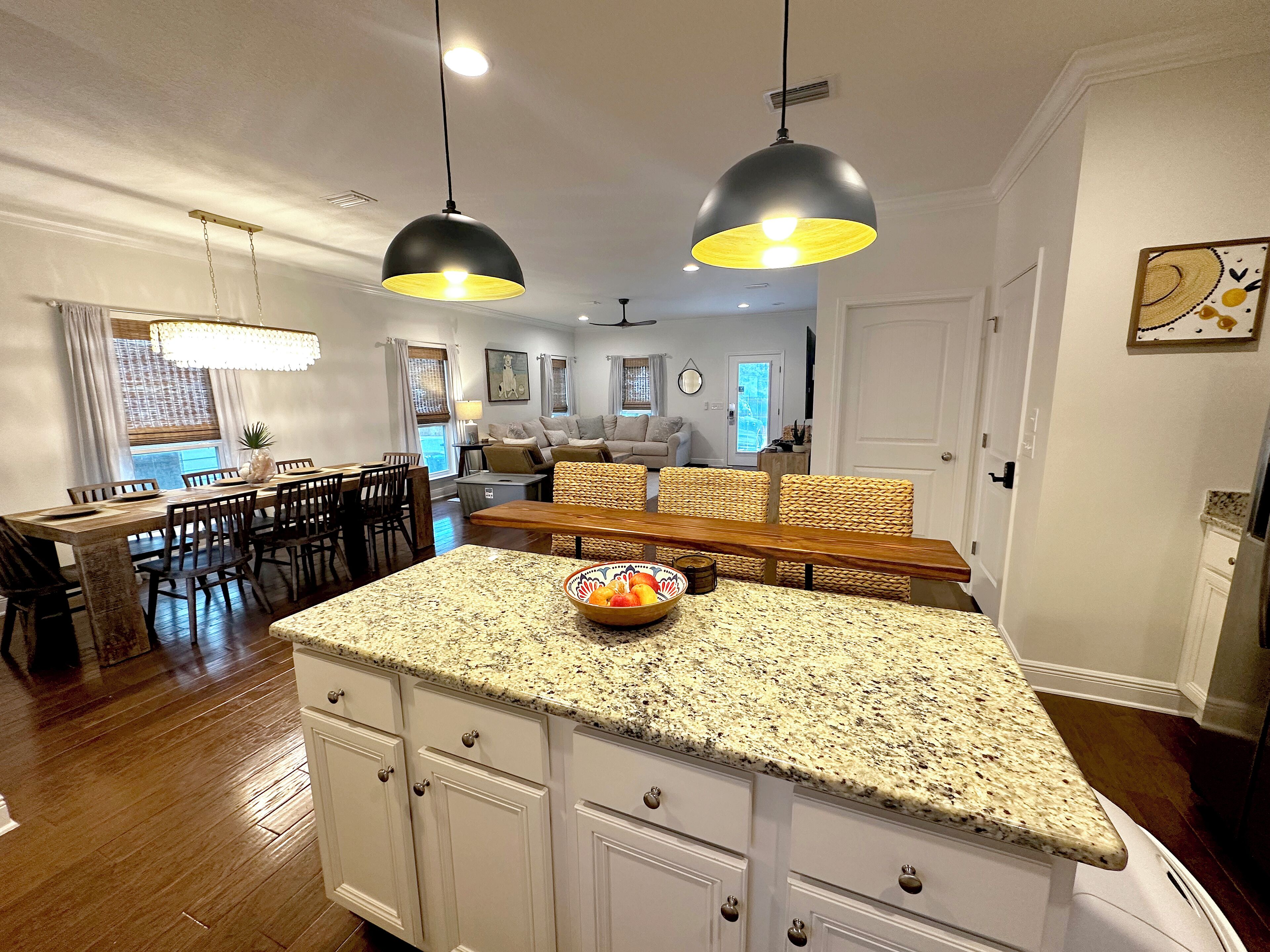 A kitchen with white cabinets, granite countertops, and a central island with a bowl of fruit. There are two pendant lights hanging above the island.