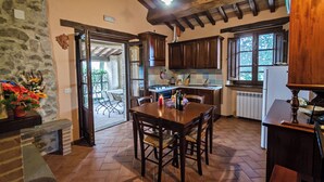 A rustic kitchen with wooden cabinets, a dining table, and a stone wall. - The Granary - Farmhouse La Fattoria (Monte Santa Maria Tiberina)