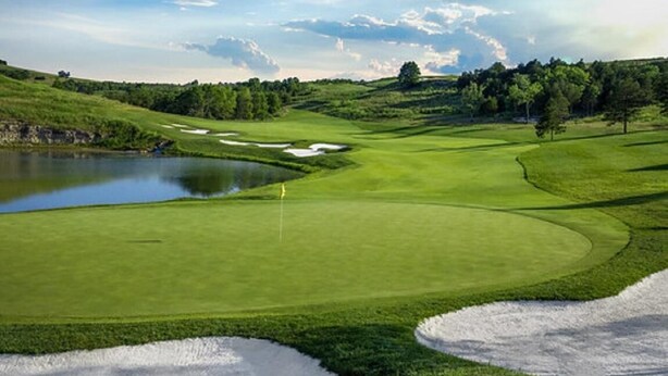 Un parcours de golf avec un étang, des bunkers de sable et un mât de drapeau.