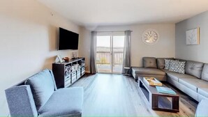 Un salon moderne avec un canapé, un fauteuil et un téléviseur à écran plat fixé au mur.