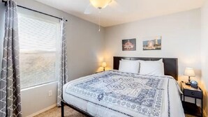 Une chambre à coucher comprenant un lit, un ventilateur de plafond, deux lampes fixées au mur et deux tableaux encadrés.