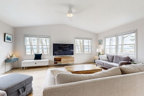 Relax in this spacious living room with a large flat-screen TV, comfortable seating, and a ceiling fan.