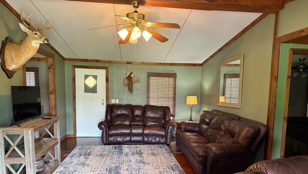 A living room with a brown leather sofa, a wooden coffee table, a ceiling fan, and a mounted deer head.