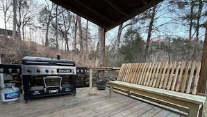 An outdoor wooden deck with a barbecue grill, a bench, and a propane tank.