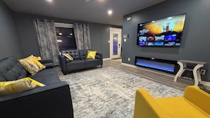 A modern living room with a black leather sofa, a yellow armchair, and a flat-screen TV mounted on the wall.