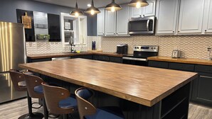 A modern kitchen with a central island, bar stools, stainless steel appliances, and pendant lighting.